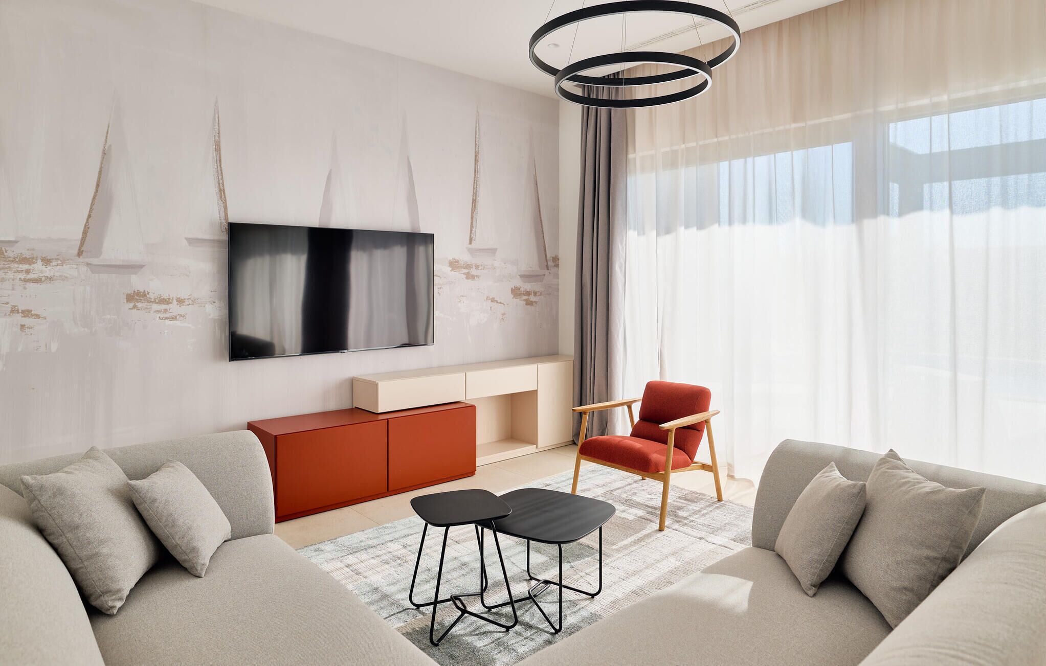 Un salon moderne avec un canapé, un fauteuil rouge, un téléviseur et un luminaire au plafond original.