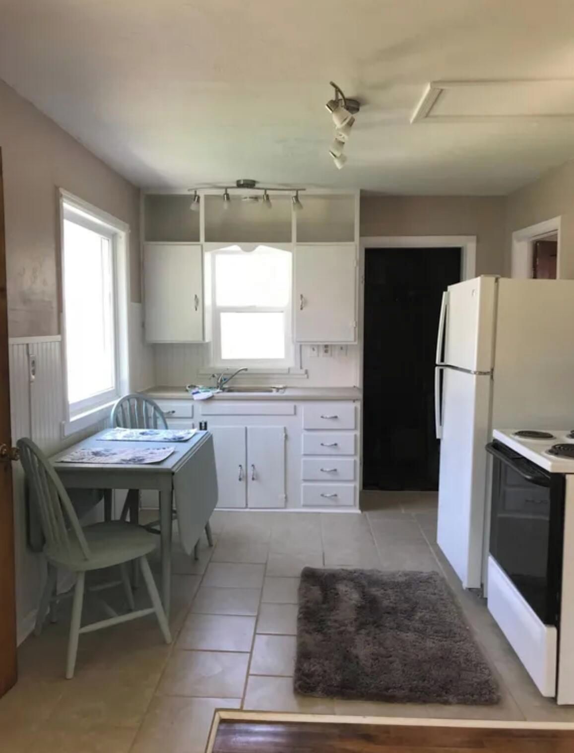 Une cuisine avec des meubles blancs, une table à manger, des chaises, un réfrigérateur et une cuisinière.