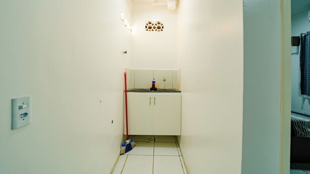 Un pasillo estrecho con un armario blanco, una escoba y un poste rojo.