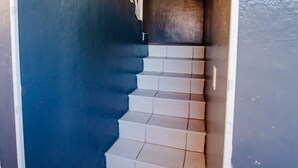 Una escalera con escalones blancos y barandilla de madera, que conduce a un espacio interior oscuro.