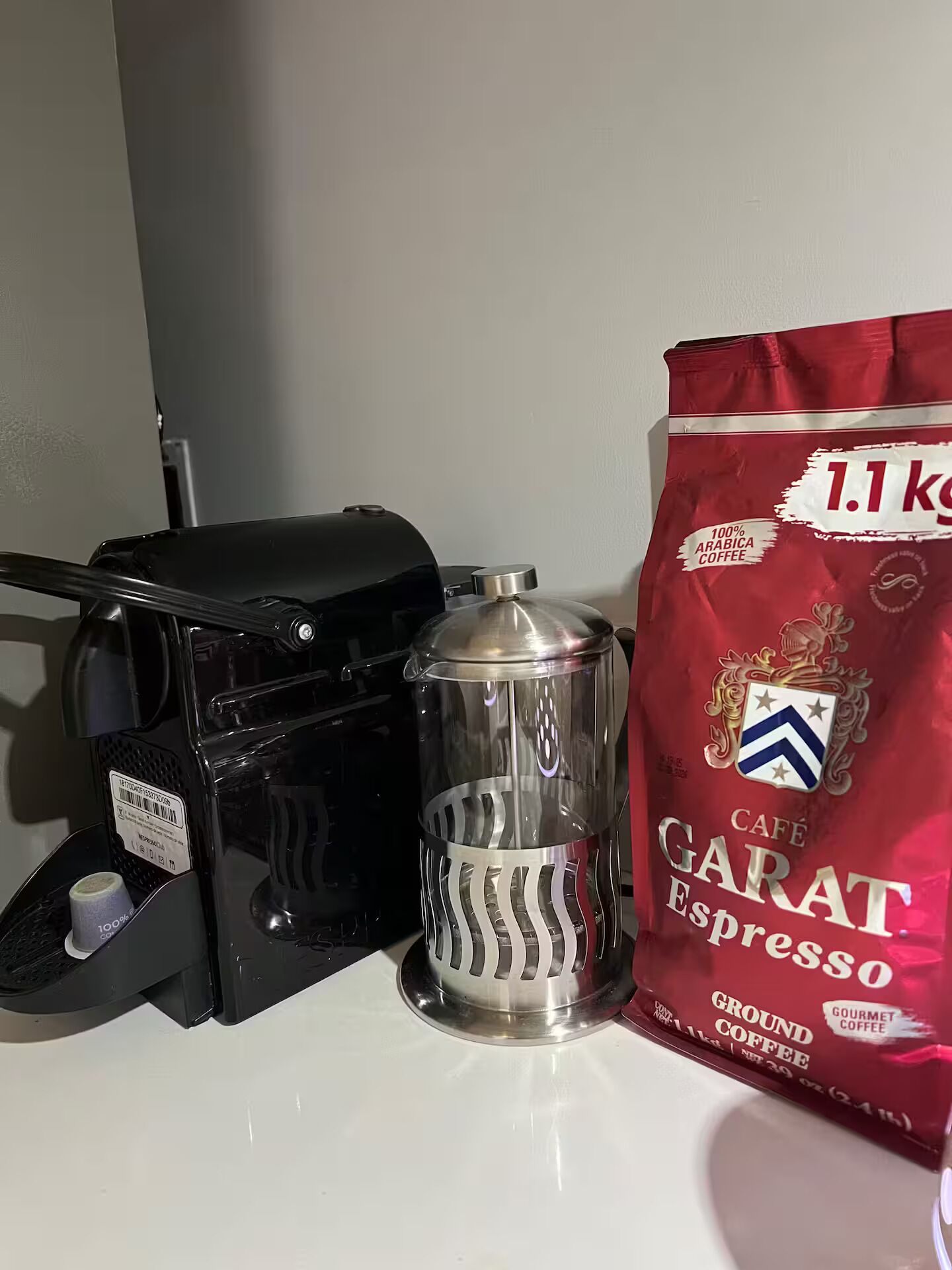 A coffee maker, a glass carafe, and a bag of Café Garat Espresso ground coffee on a white surface.