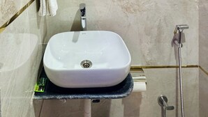A bathroom with a white sink, a mirror, a towel rack, and a shower. - Hotel Classic Crowne (New Delhi)