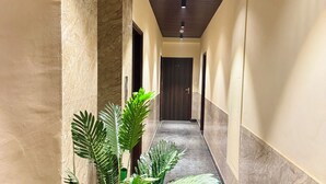 A hallway with a marble floor, a wooden ceiling, and a potted plant. - Hotel Classic Crowne (New Delhi)