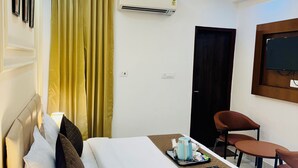 A hotel room with a bed, bedside lamp, air conditioning unit, ceiling fan, and a TV mounted on the wall.