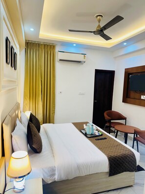 A hotel room with a bed, bedside lamp, air conditioning unit, ceiling fan, and a TV mounted on the wall. - Hotel Classic Crowne (New Delhi)