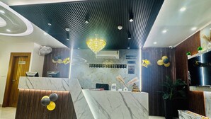 A reception desk with a marble top, a wooden panel design, and a chandelier. There is a sign that reads "HAPPY NEW YEAR" and a "CHECK IN/ CHECK OUT" sign.