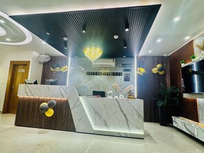 A reception desk with a marble top, a wooden panel design, and a chandelier. There is a sign that reads "HAPPY NEW YEAR" and a "CHECK IN/ CHECK OUT" sign. - Hotel Classic Crowne (New Delhi)