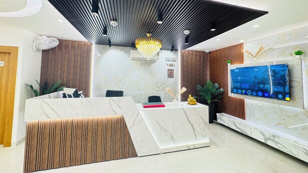 A modern reception area with a marble reception desk, a large flat-screen TV, and a chandelier.