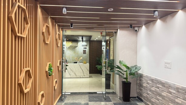 A modern reception area with a check-in desk, a glass partition, and a potted plant. - Hotel Classic Crowne (New Delhi)