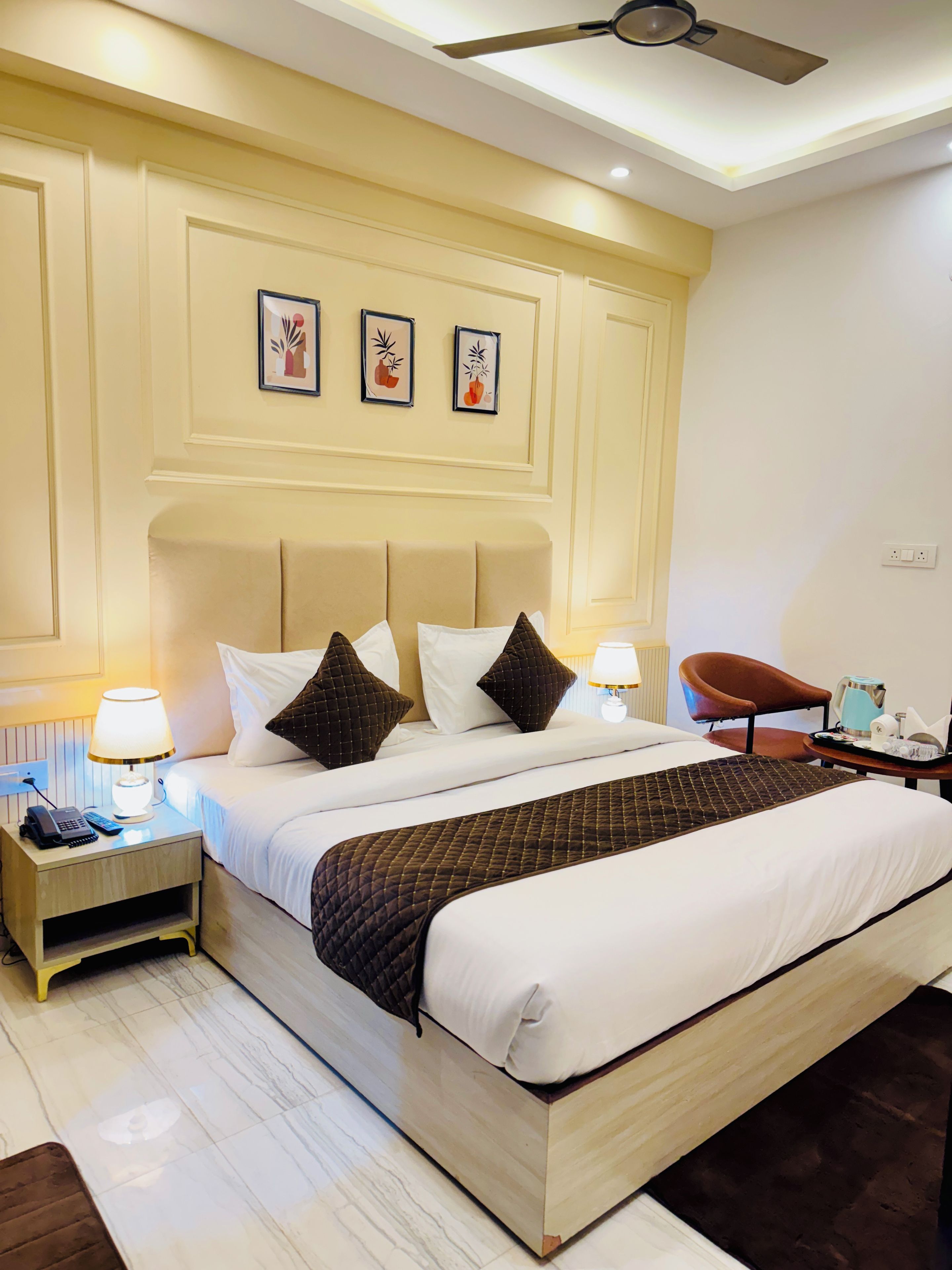 A hotel room with a large bed, bedside tables with lamps, a ceiling fan, and framed artwork on the wall.