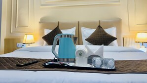 A hotel room with a bed, a tray with a kettle, cups, and a remote control. There are three framed pictures on the wall above the bed.