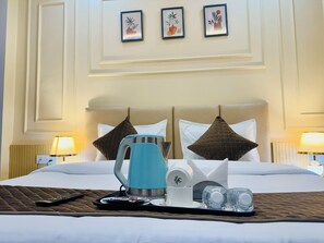 A hotel room with a bed, a tray with a kettle, cups, and a remote control. There are three framed pictures on the wall above the bed. - Hotel Classic Crowne (New Delhi)
