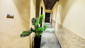A hallway with a marble floor, a potted plant, and a ceiling with a textured pattern. - Hotel Classic Crowne (New Delhi)