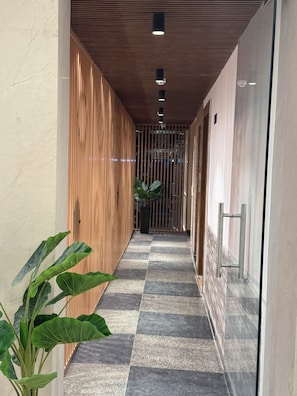 A corridor with a checkered floor, wooden paneling on one side, and a potted plant. - Hotel Classic Crowne (New Delhi)