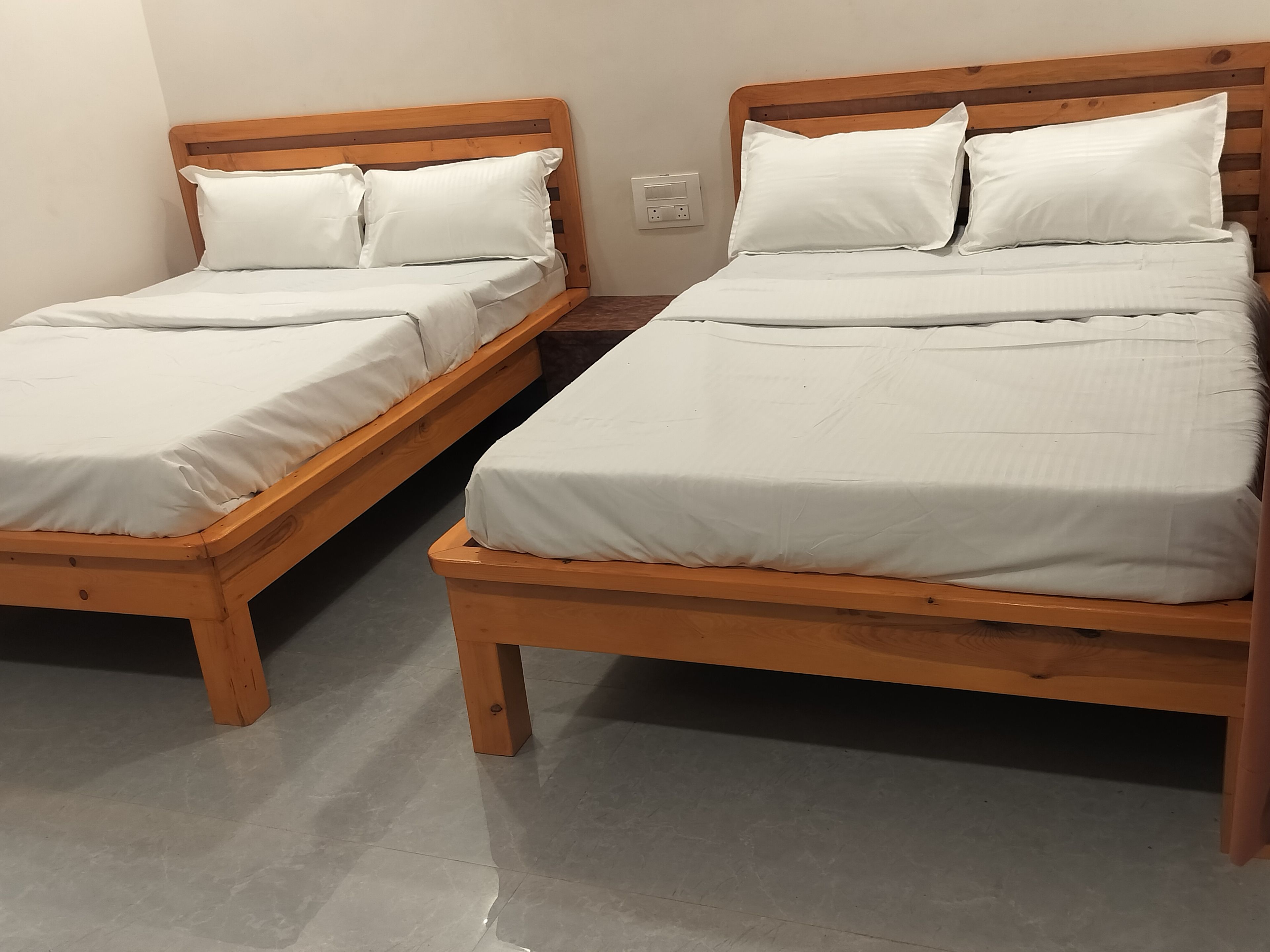 Two wooden beds with white bedding in a room with a tiled floor.