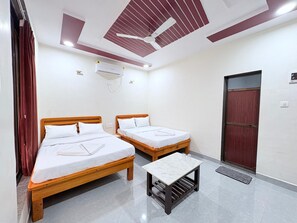A room with two wooden beds, a small table, a ceiling fan, an air conditioning unit, and a door. - Sandalwoods Resorts (Karjat)