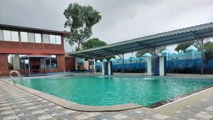 A swimming pool with a tiled deck, a covered area with a mural, and a building with large windows.