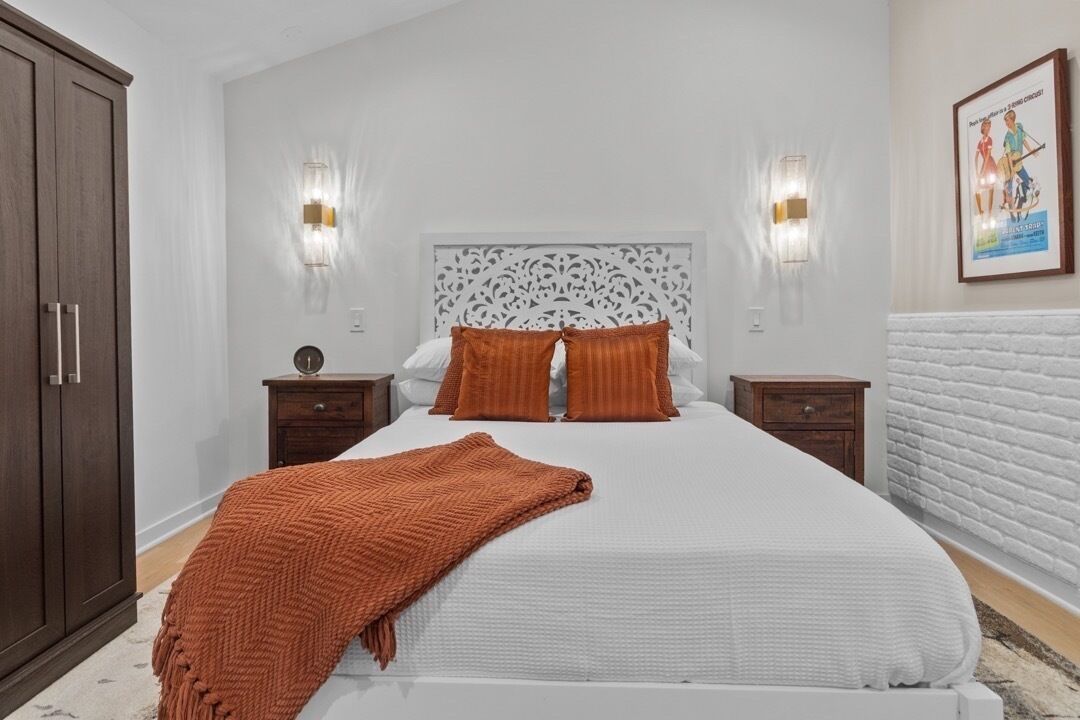 A bedroom with a large bed, two nightstands, a wardrobe, and decorative wall sconces.