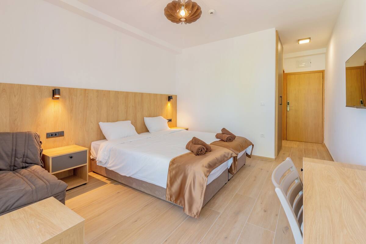 A modern hotel room with a bed, bedside tables, a chair, and a wooden floor.