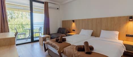 A modern hotel room with a large bed, a desk, and a balcony with chairs.