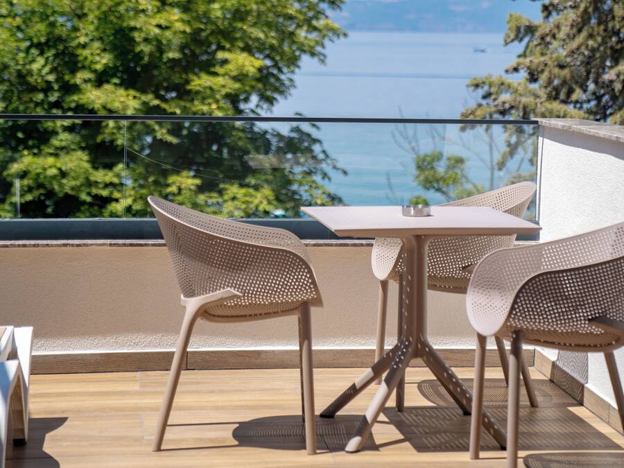 Un balcón al aire libre con una mesa y sillas, con vista a un cuerpo de agua y árboles.