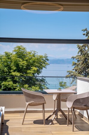 Un balcon extérieur avec une table et des chaises, donnant sur une étendue d’eau et des arbres.