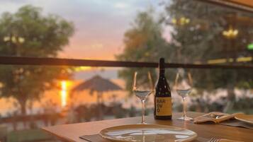 A dining table set with plates, cutlery, and a bottle of Barovivo wine, with a view of trees and a sunset through a window.