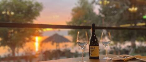 A dining table set with plates, cutlery, and a bottle of Barovivo wine, with a view of trees and a sunset through a window.