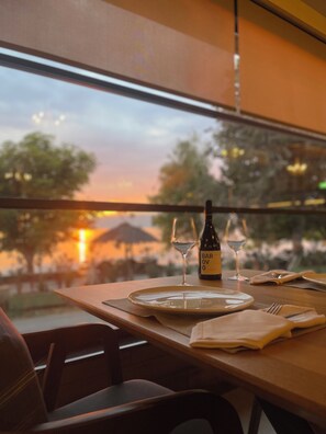 A dining table set with plates, cutlery, and a bottle of Barovivo wine, with a view of trees and a sunset through a window.