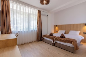 A hotel room with a wooden floor, a bed with white bedding, a wooden headboard, a desk with a chair, and a window with sheer curtains. - Lago Hotel & Spa (Ohrid)