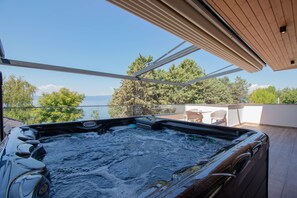 Un jacuzzi sur un balcon offrant une vue dégagée sur la mer et les arbres.
