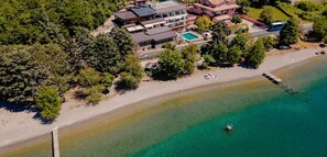 An aerial view of a coastal property with a large house, a swimming pool, and a beach.