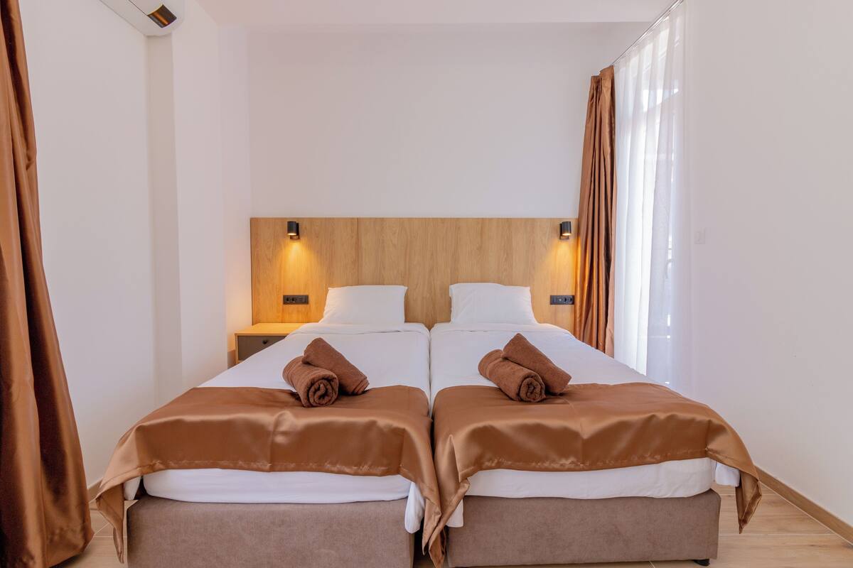 A twin room with two beds, a wooden headboard, bedside lamps, and brown curtains.