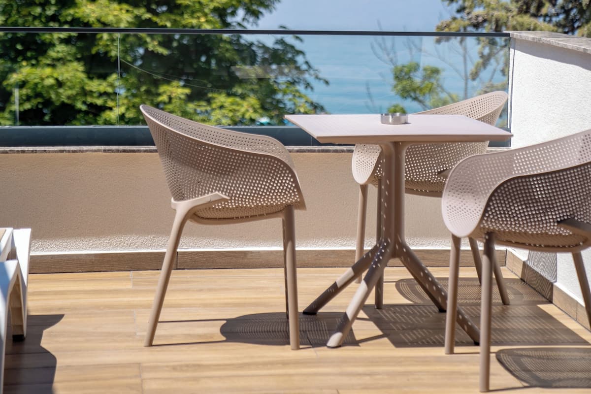 An outdoor balcony with a table and chairs, overlooking a body of water and trees.
