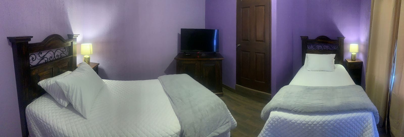 A hotel room with two single beds, a television on a wooden stand, and a door in the background.