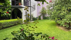 Un jardín cuidado con diversas plantas y flores, césped recién cortado y un balcón con iluminación exterior.