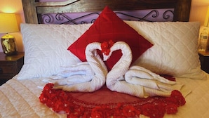 Una cama con una colcha acolchada, un almohá de color rojo y dos toallas dispuestas en forma de corazón.