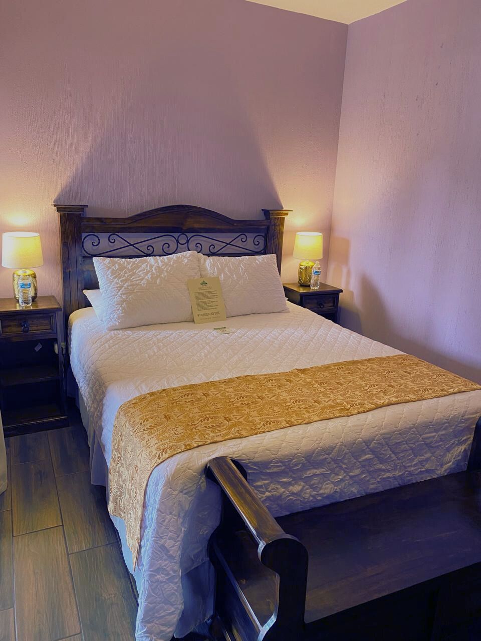 A neatly made bed with a headboard, two bedside tables with lamps, and a wooden bench at the foot of the bed.