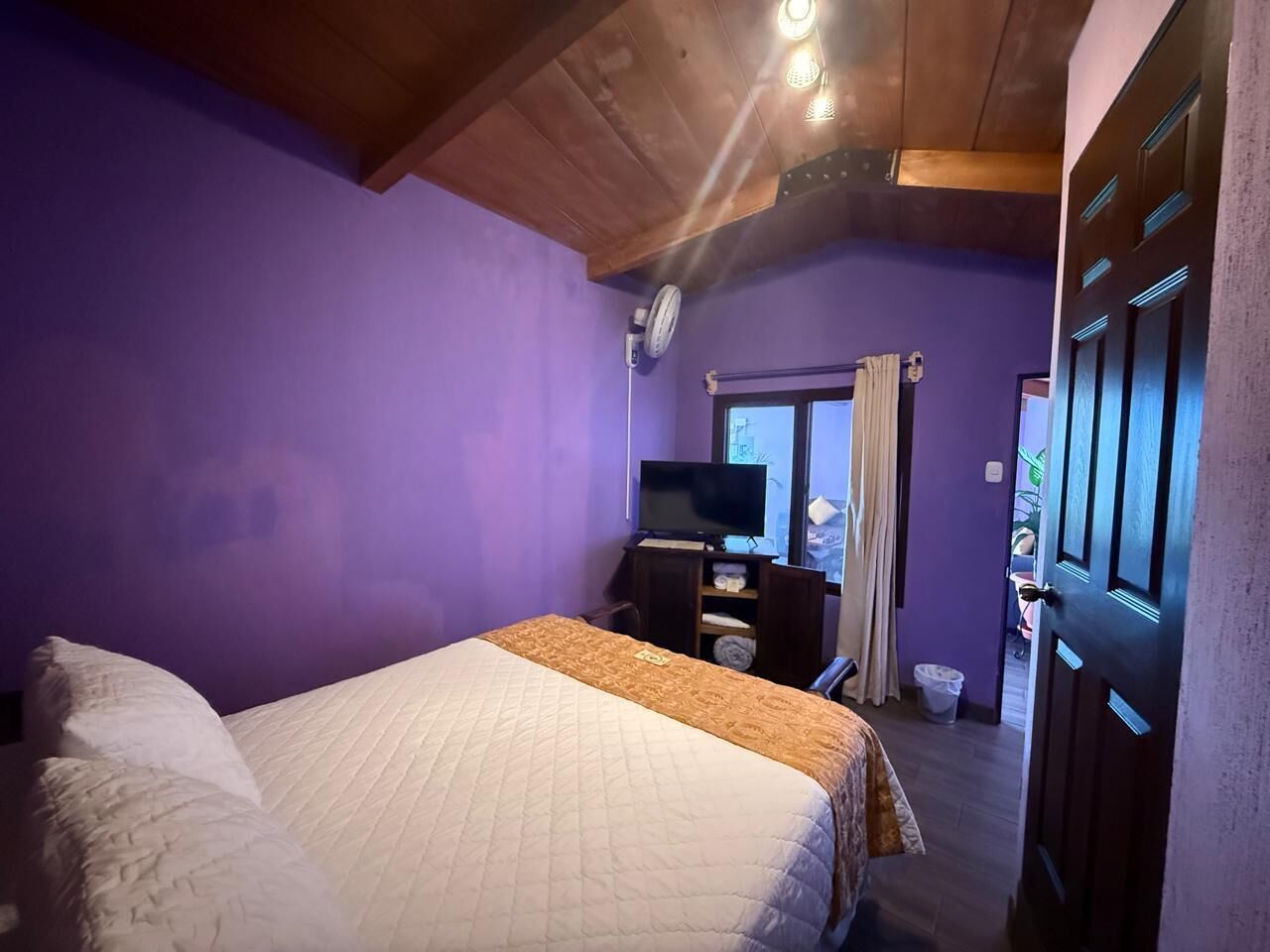 A bedroom with a bed, a dresser, a television, and a window with curtains.