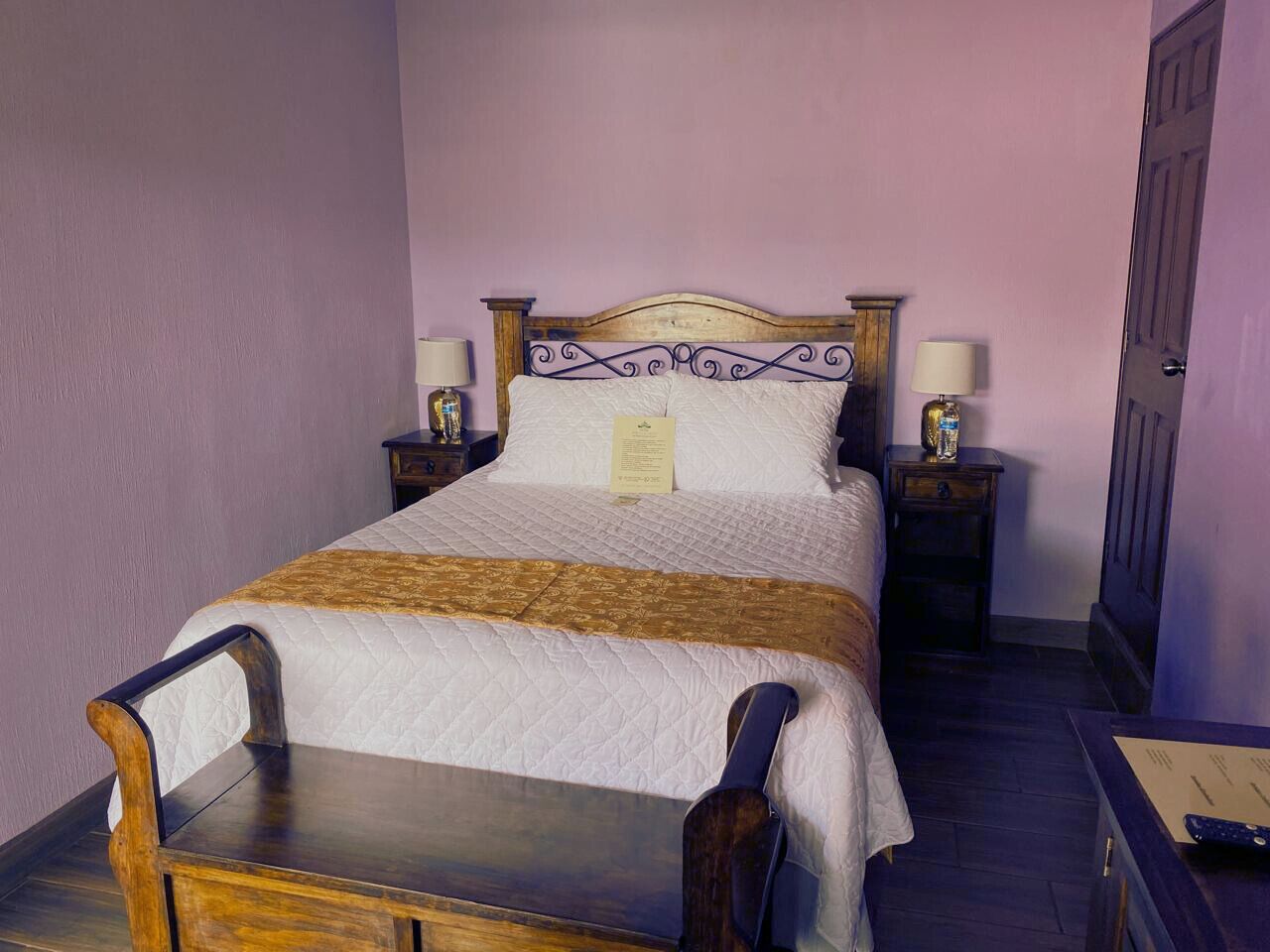 A neatly made bed with a wooden headboard, two bedside tables with lamps, and a small wooden table in front of the bed.