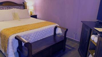 A neatly made bed with a wooden headboard, a bedside table with a lamp, and a bench at the foot of the bed.