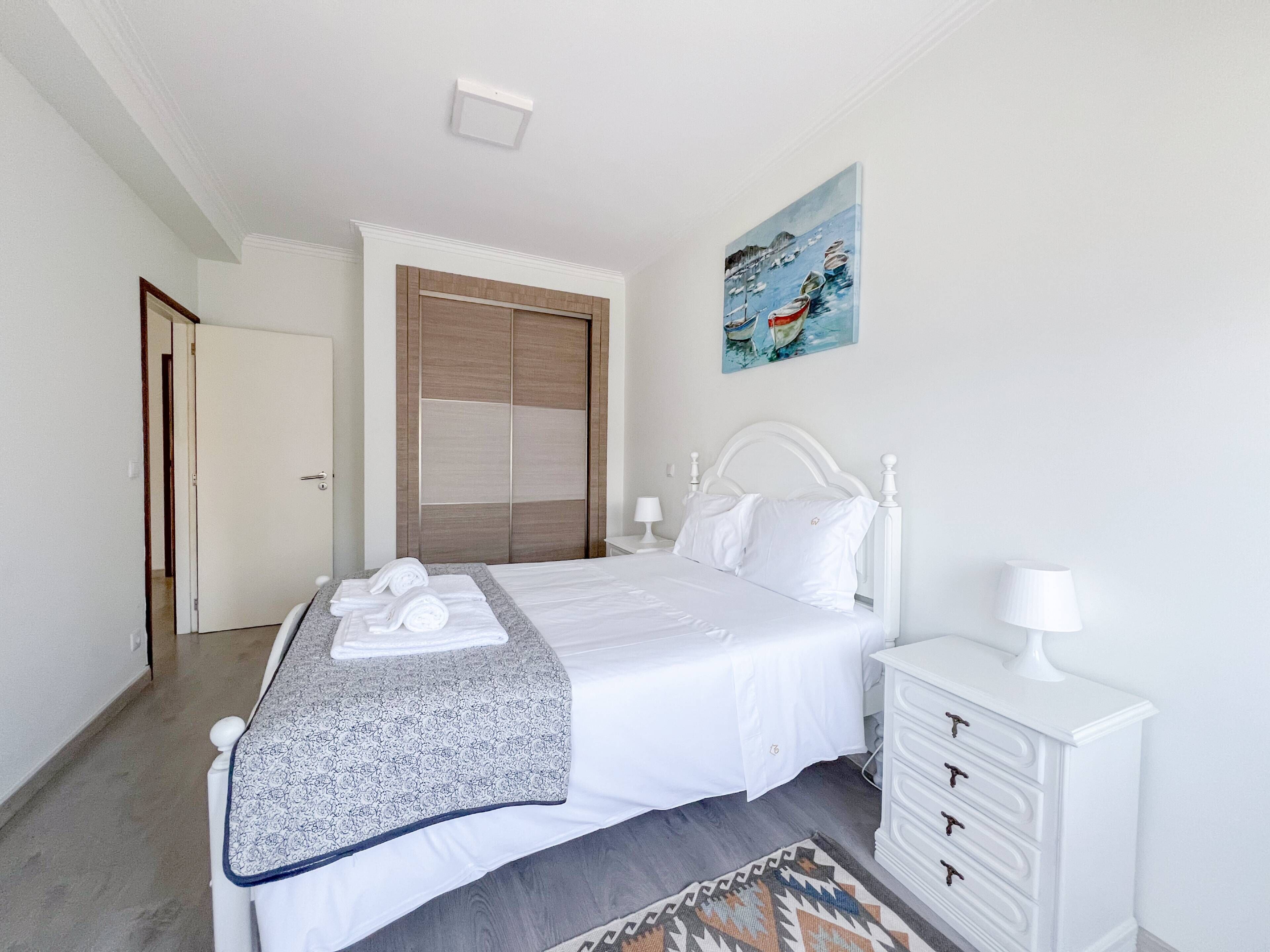 A neatly arranged bedroom with a bed, a dresser, a painting, and a door.