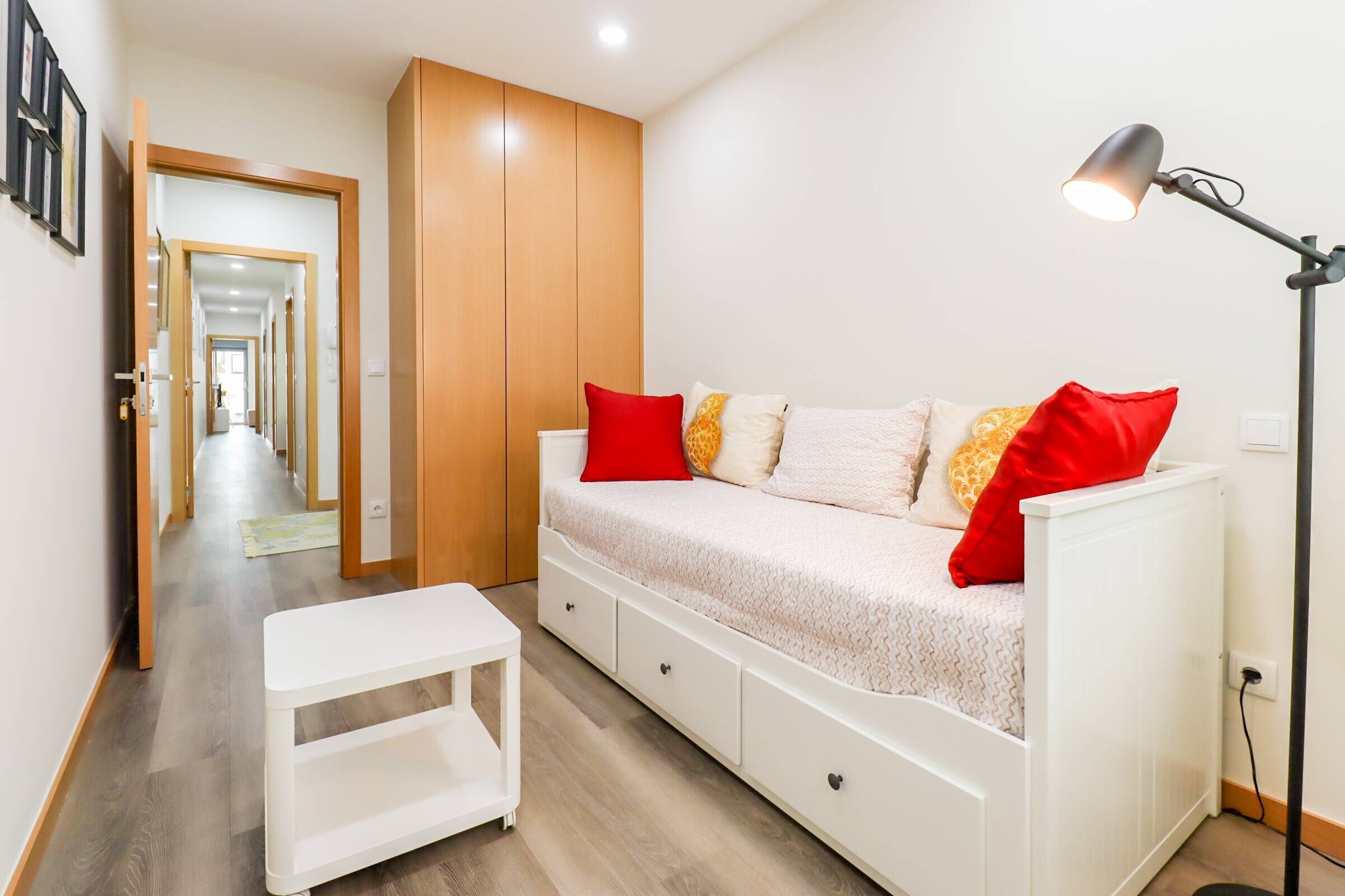A bedroom with a bed, bedside table, lamp, and a view of a hallway.