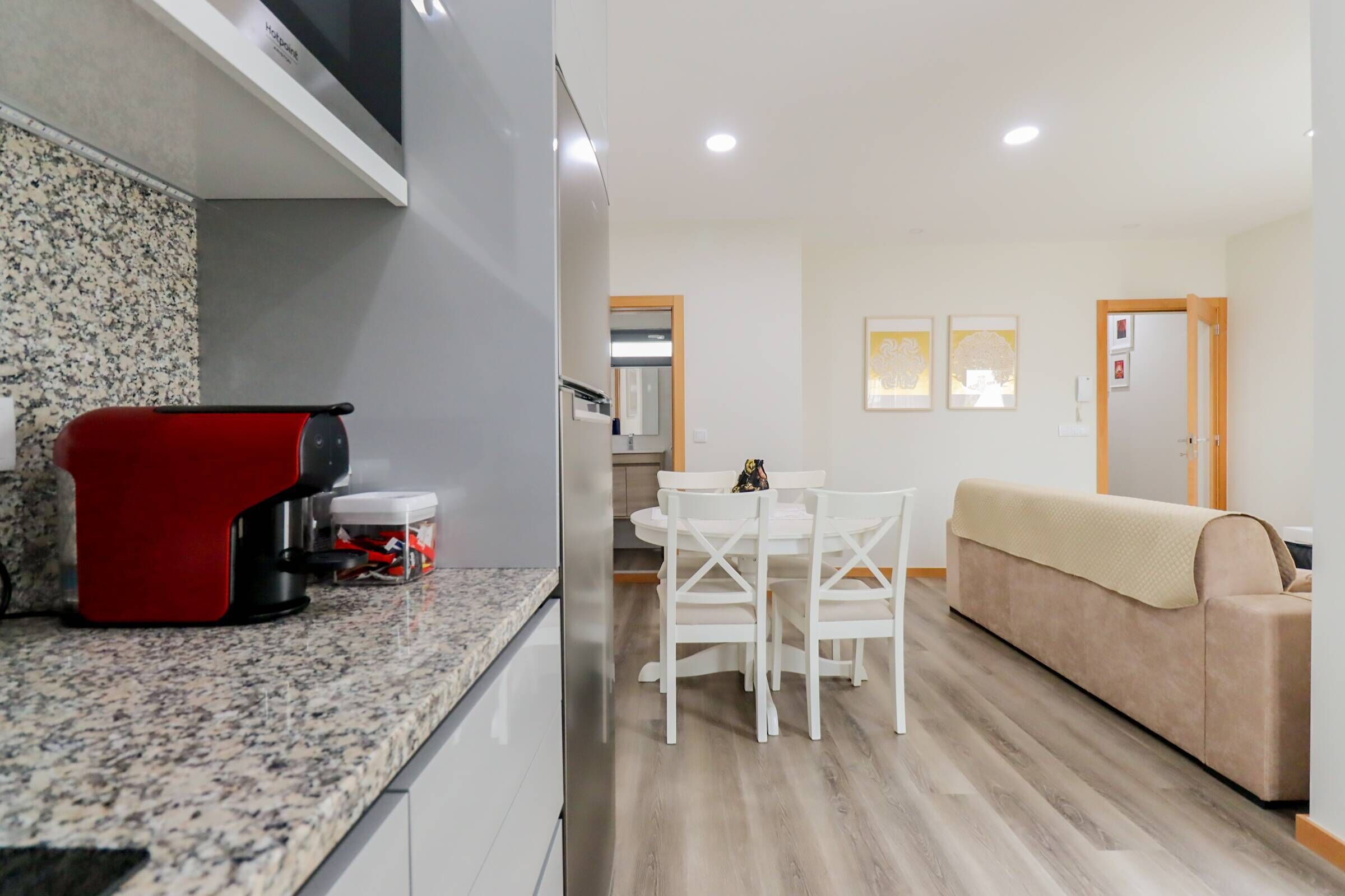 Cozinha moderna com bancadas de granito, um eletrodoméstico vermelho e um espaço de refeições com cadeiras brancas e uma mesa.