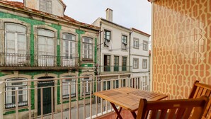 A balcony with a wooden table and chairs, overlooking a street with historic buildings.