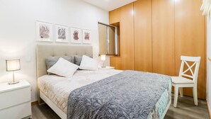 A bedroom with a bed, bedside tables, a chair, a wardrobe, and framed artwork on the wall.