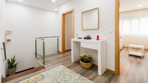 A modern hotel room with a white console table, a mirror, a small plant, and a wooden-framed door.
