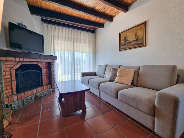 Una sala de estar con chimenea de ladrillo, un televisor de pantalla plana, un sofá y un cuadro en la pared.