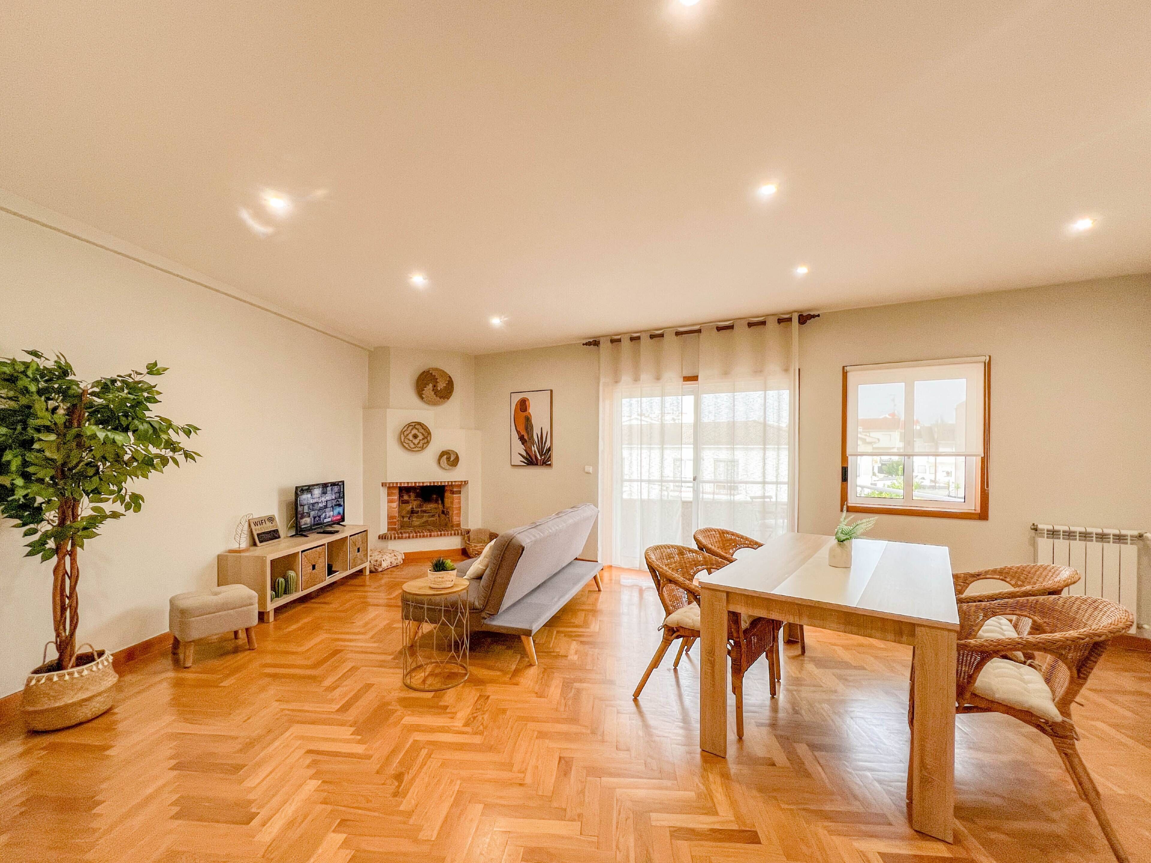Un'ampia zona giorno con pavimento in parquet a spina di pesce, un camino, un divano, un tavolo da pranzo con sedie e un'ampia finestra con tende.