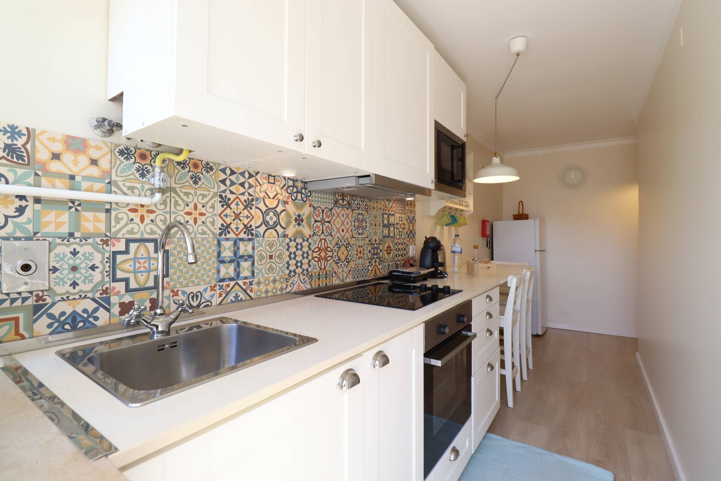 A compact kitchen with white cabinets, a tiled backsplash, a stainless steel sink, and a built-in oven.